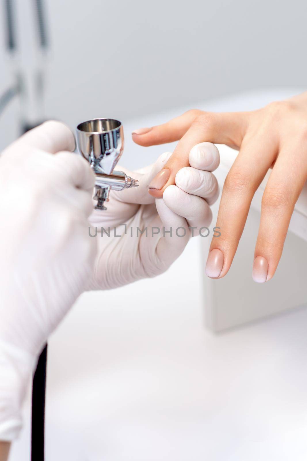 Young woman receiving manicure by airbrush in nail salon. Procedure for spraying paint on the nails