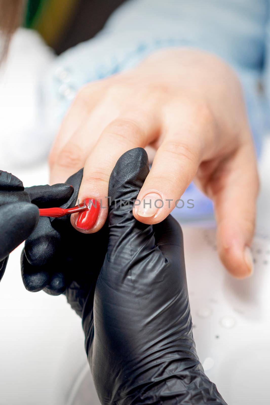 Professional manicure master painting female nails by red nail polish in nail salon