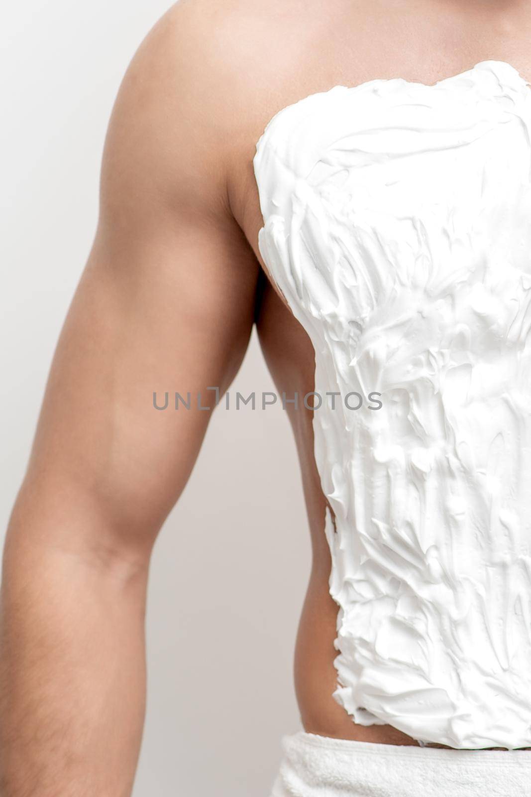 Young caucasian man with beard holds razor shaves his chest with white shaving foam on white background. Man shaving his torso