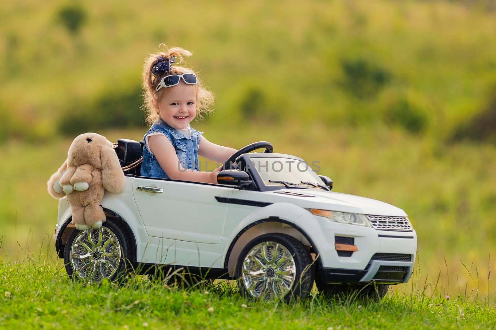 little girl rides on a children's car on a green lawn