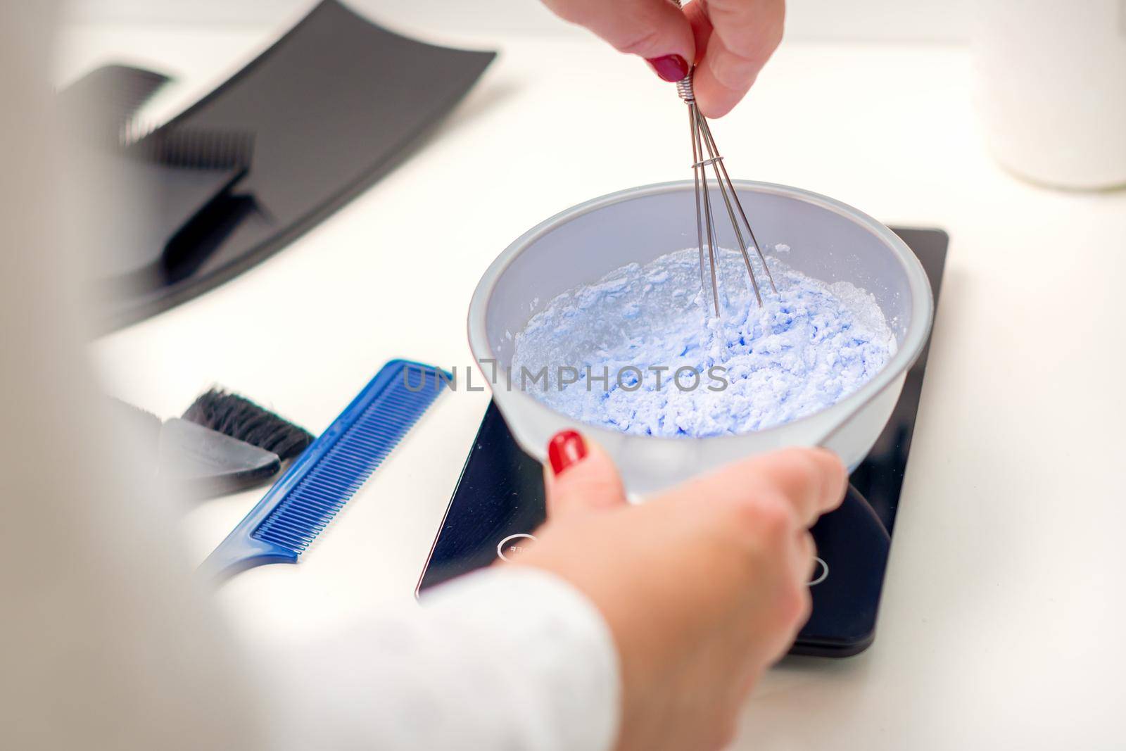 Hairdresser is mixing dye in white bowl for hair coloring in her hands