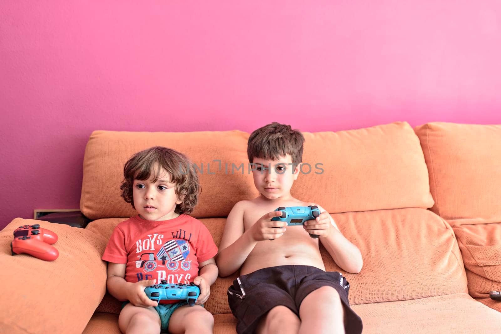 Computer game competition. Gaming concept. Excited children leaning on the sofa back playing video game with joysticks