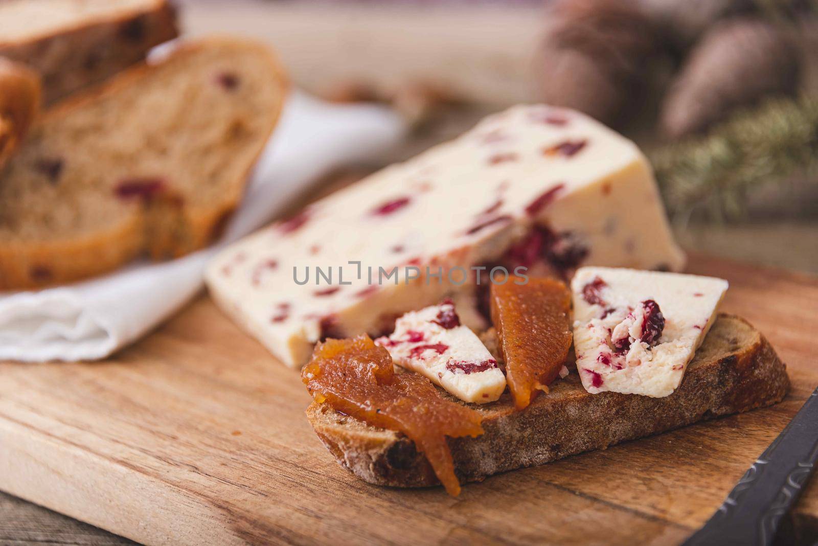 Wensleydale cheese with cranberries, red wine, honey, nuts, raisins on marble cutting board. Black concrete background. Selective focus