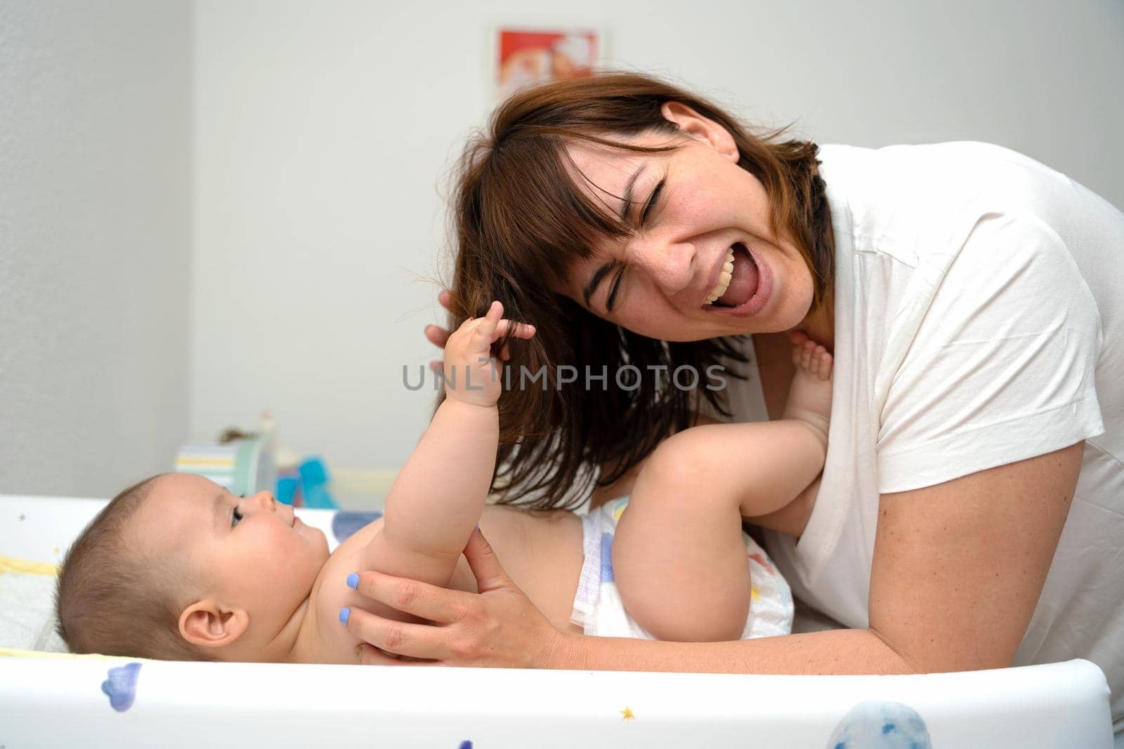 Brunette mother holding baby tight in her arms. Baby pulling and playing with mother's hair.