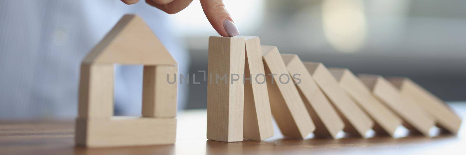 Persons hand stops wooden dominoes from falling on wooden house model by kuprevich