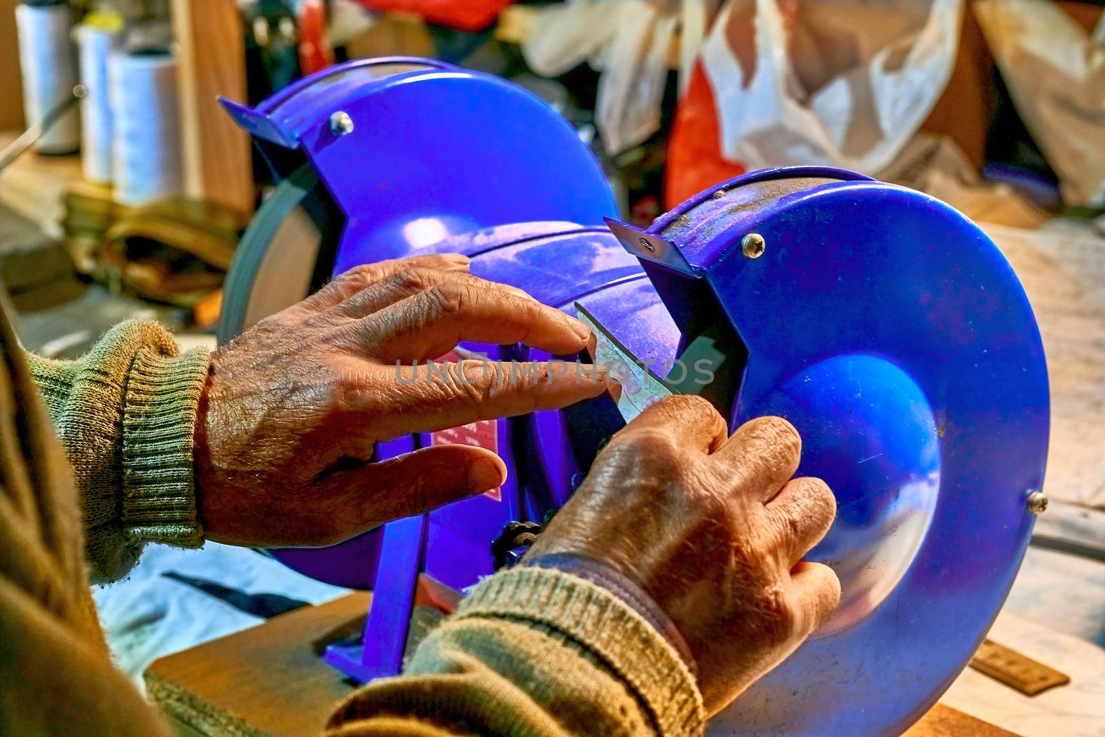 Hands of an elderly man sharpening a knife on a blue grinder by jovani68