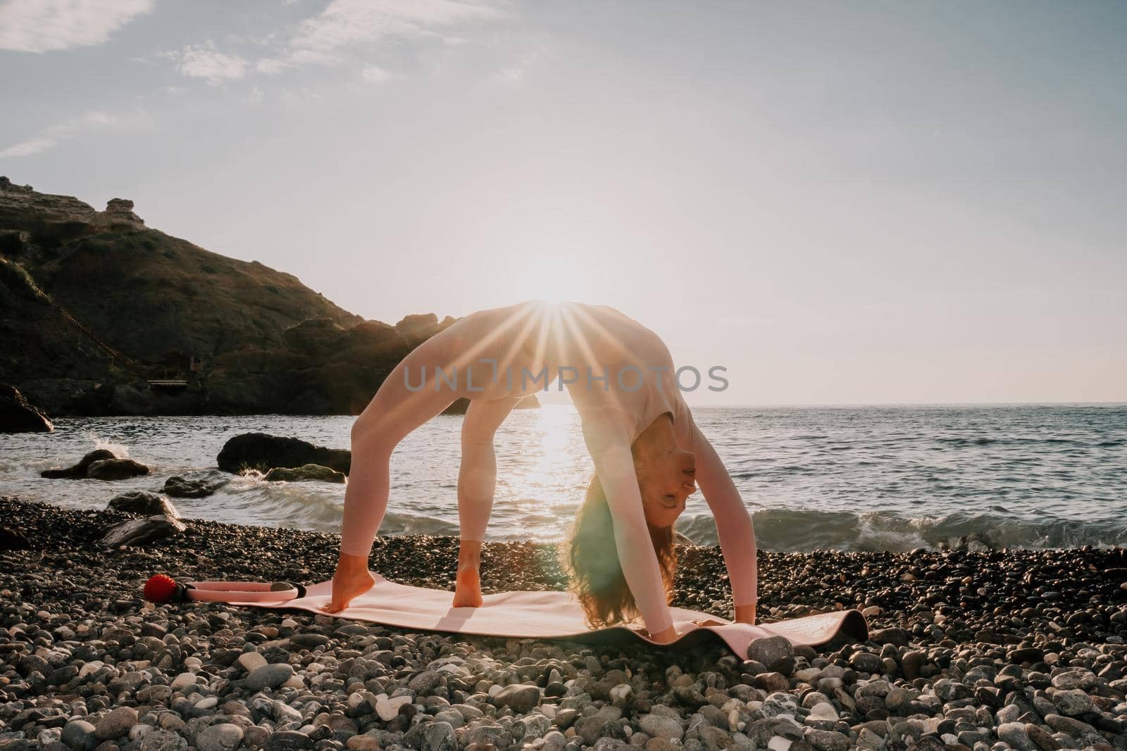 Middle aged well looking woman with black hair doing Pilates with the ring on the yoga mat near the sea on the pebble beach. Female fitness yoga concept. Healthy lifestyle, harmony and meditation. by panophotograph