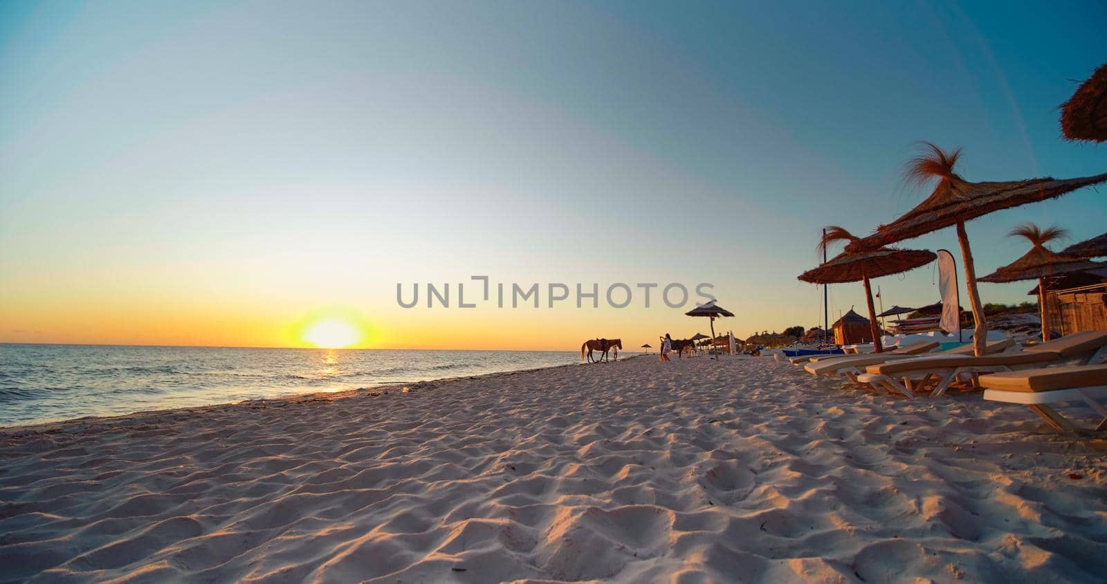 Monastir, Tunisia, 2022: Luxury summer beach resort. Beach reed umbrella from Tunisia. Sea water on the sunset. Vacation and travel concept.