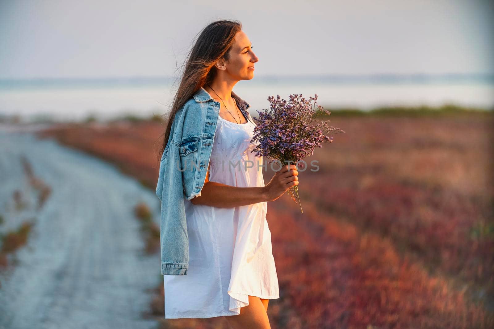 Woman with a bouquet of flowers walking on the road against the background of the sea