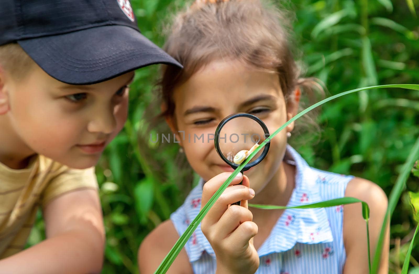 The child looks at the snail through a magnifying glass. Selective focus. Nature.