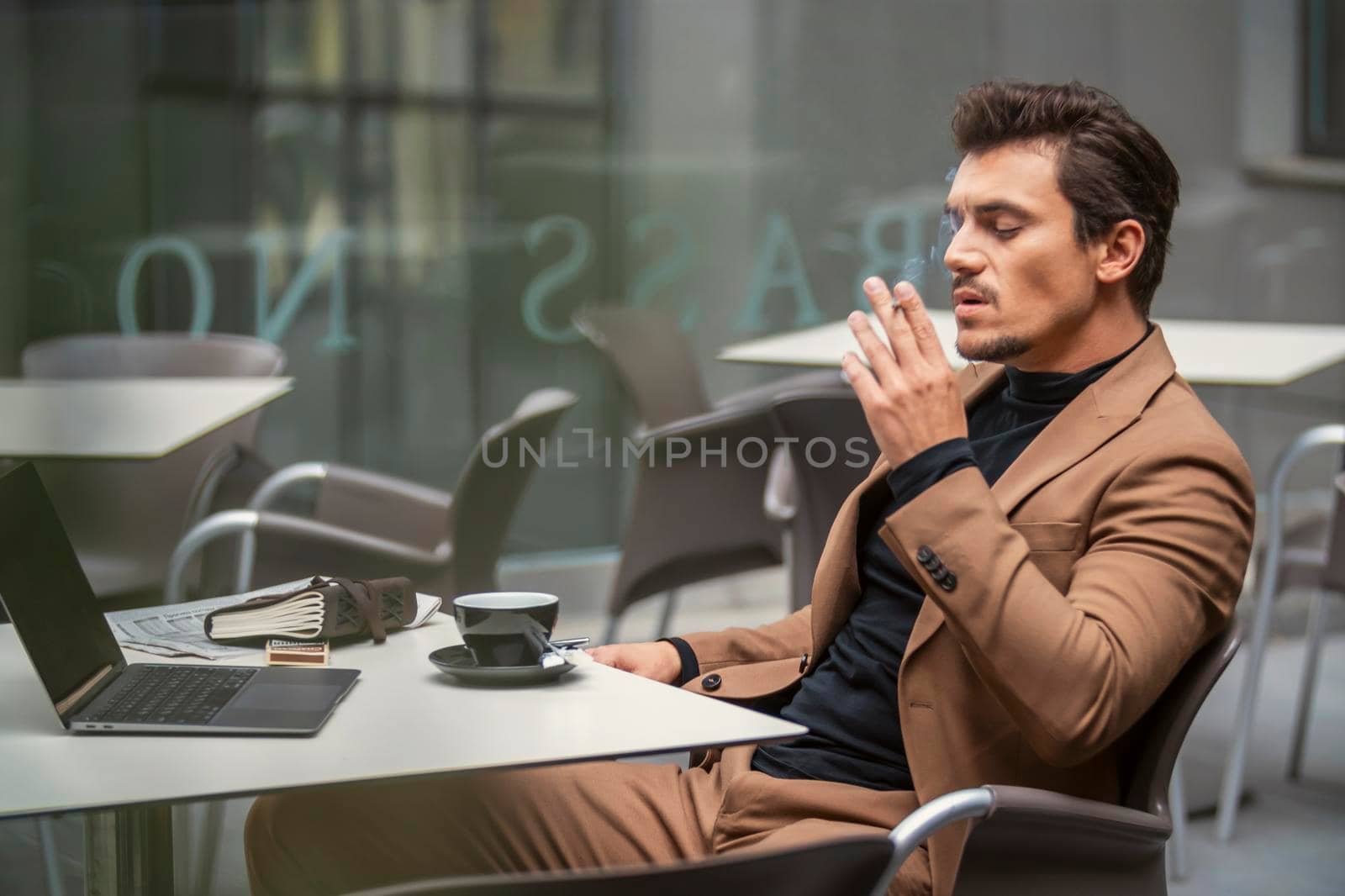 a man in a suit sits at a table and smokes