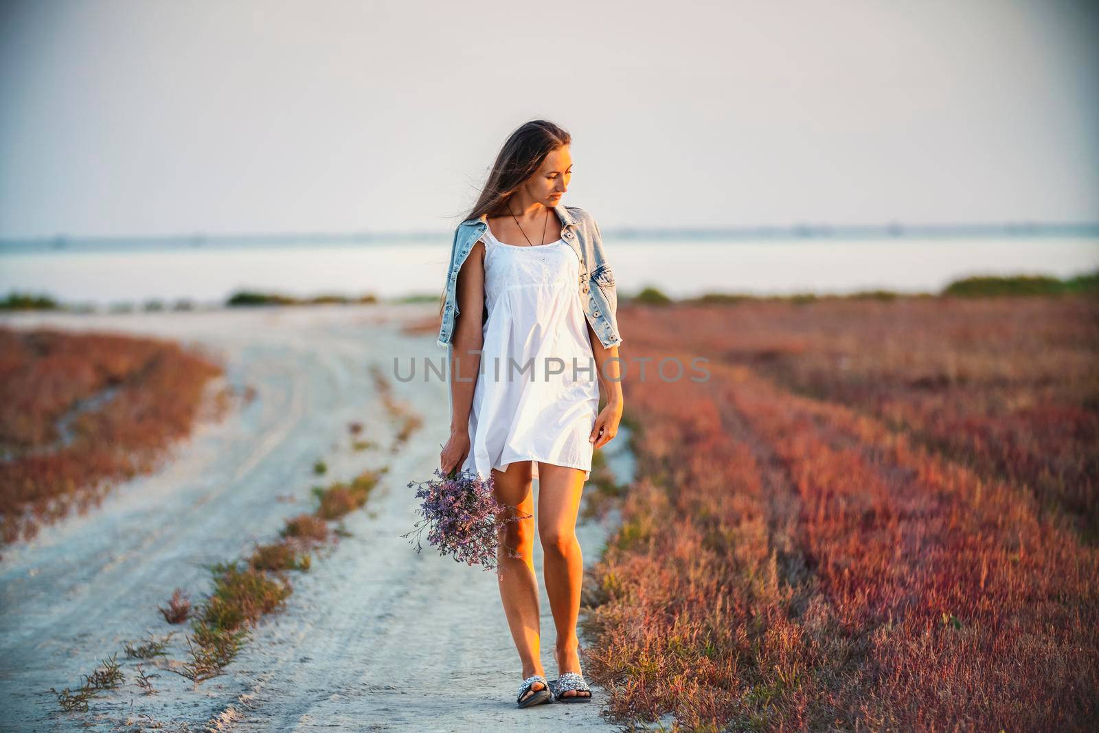 Woman with a bouquet of flowers walking on the road against the background of the sea