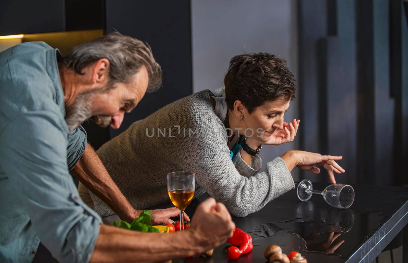 aged couple in the kitchen talking about something while drinking wine