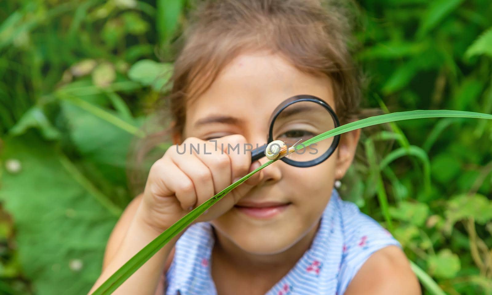 The child looks at the snail through a magnifying glass. Selective focus. Nature.