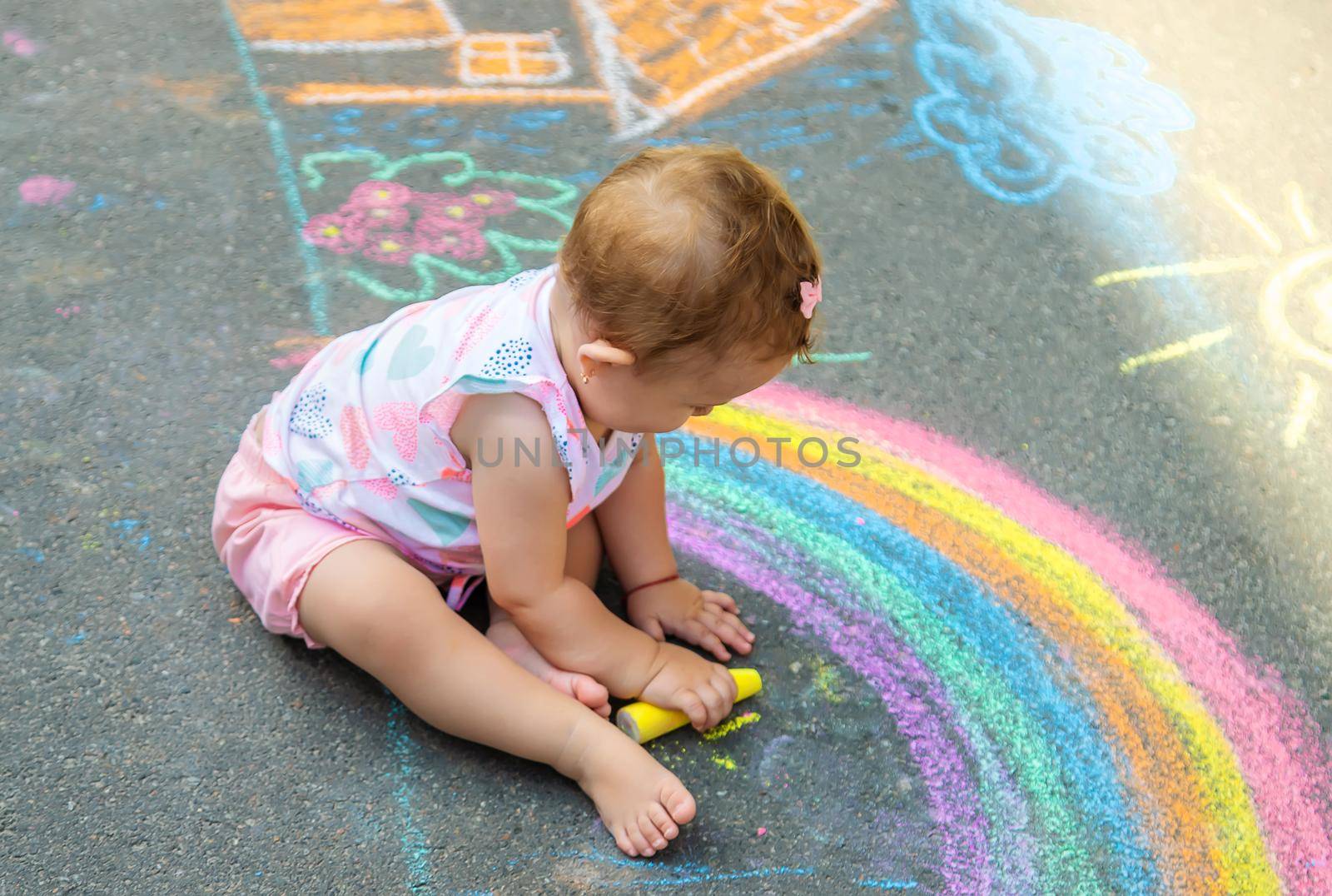 The child draws a house and a rainbow on the asphalt with chalk. Selective focus. Kids.