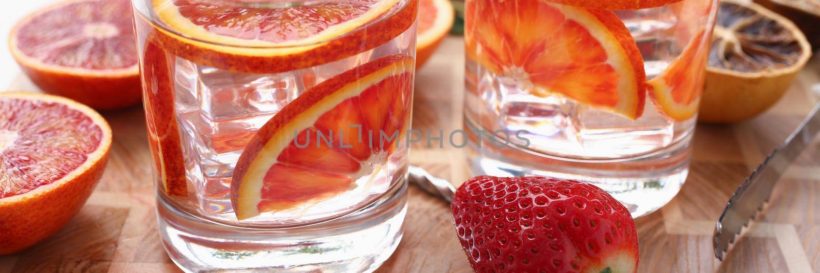 Close-up of orange punch with green mint served with strawberry on wooden table. Fresh summer cocktail with grapefruit and ice cubes. Drink, party concept