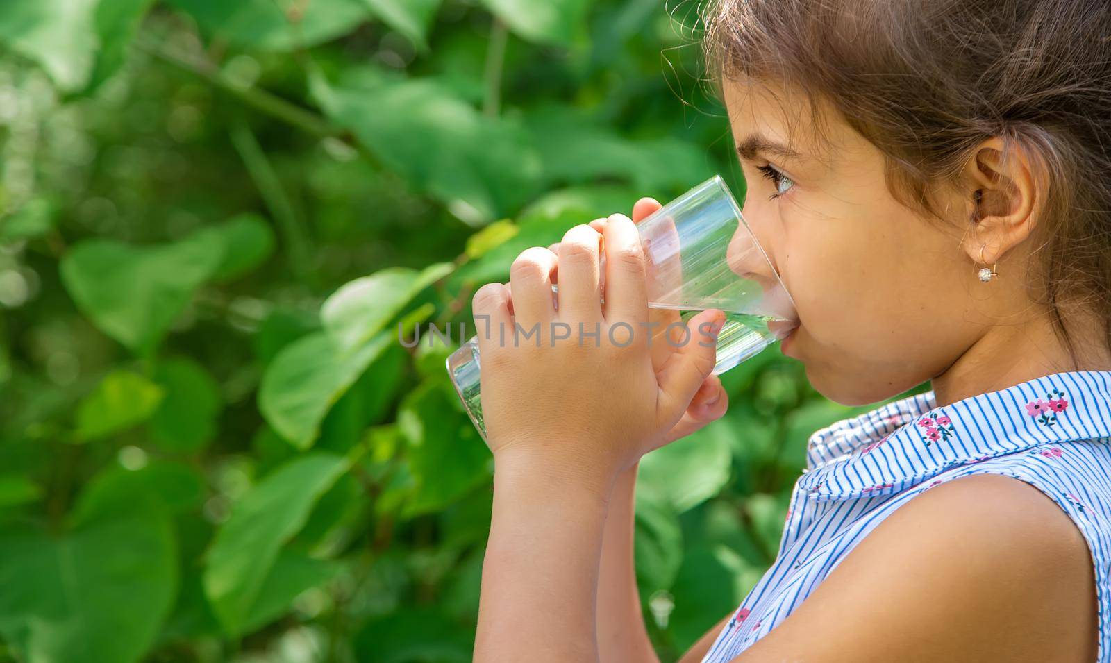 Child girl drinks water from a glass. Selective focus. Kid.