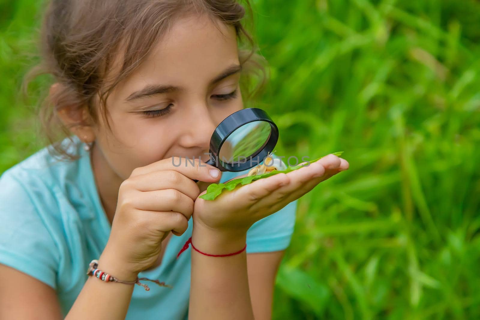 The child looks at the snail through a magnifying glass. Selective focus. by yanadjana