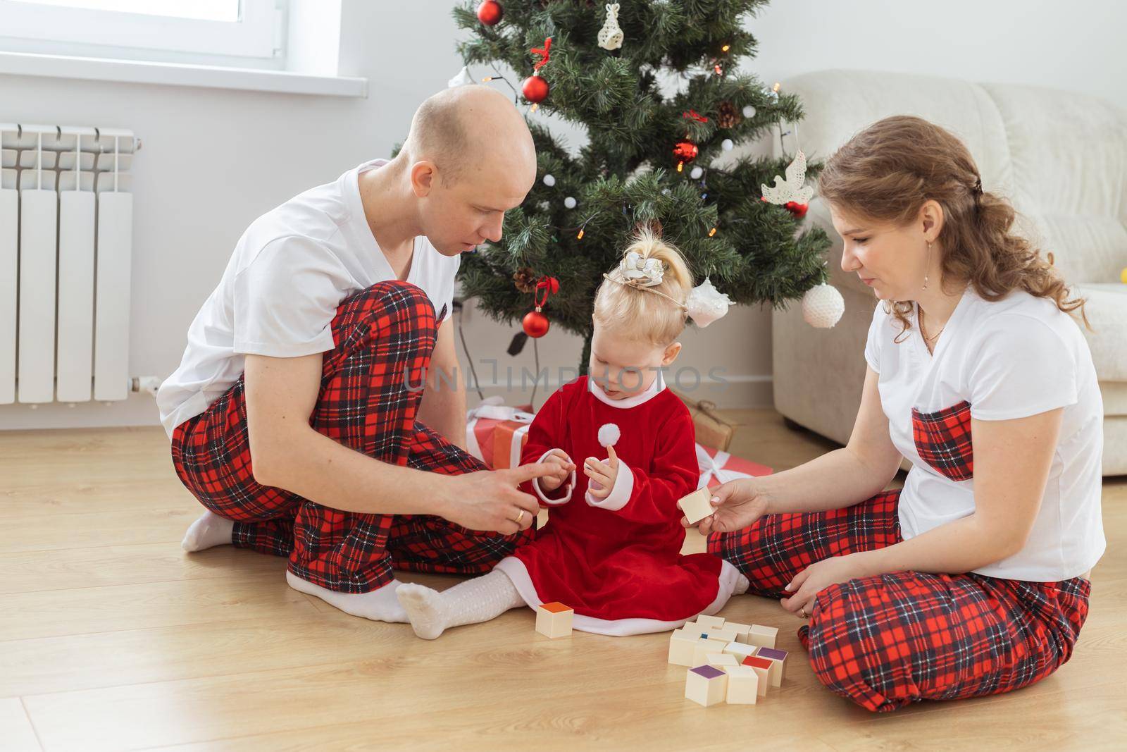 Toddler child with cochlear implant plays with parents under christmas tree - deafness and innovating medical technologies for hearing aid and diversity by Satura86