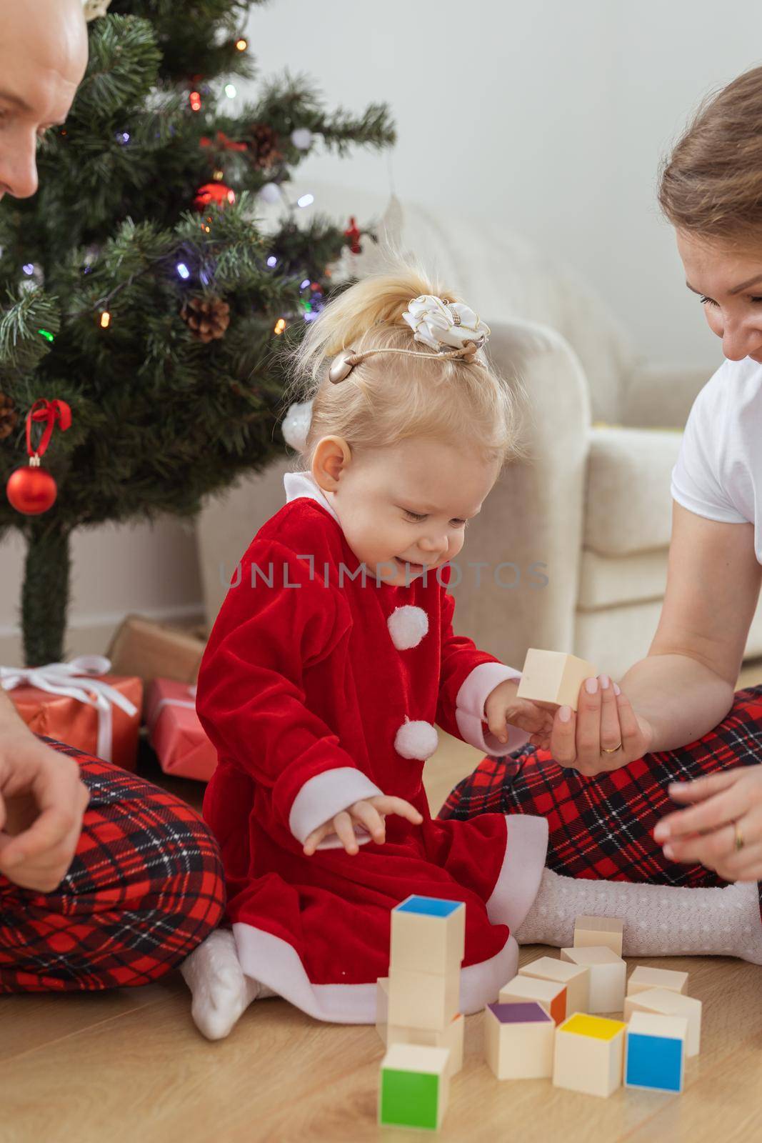 Toddler child with cochlear implant plays with parents under christmas tree - deafness and innovating medical technologies for hearing aid by Satura86