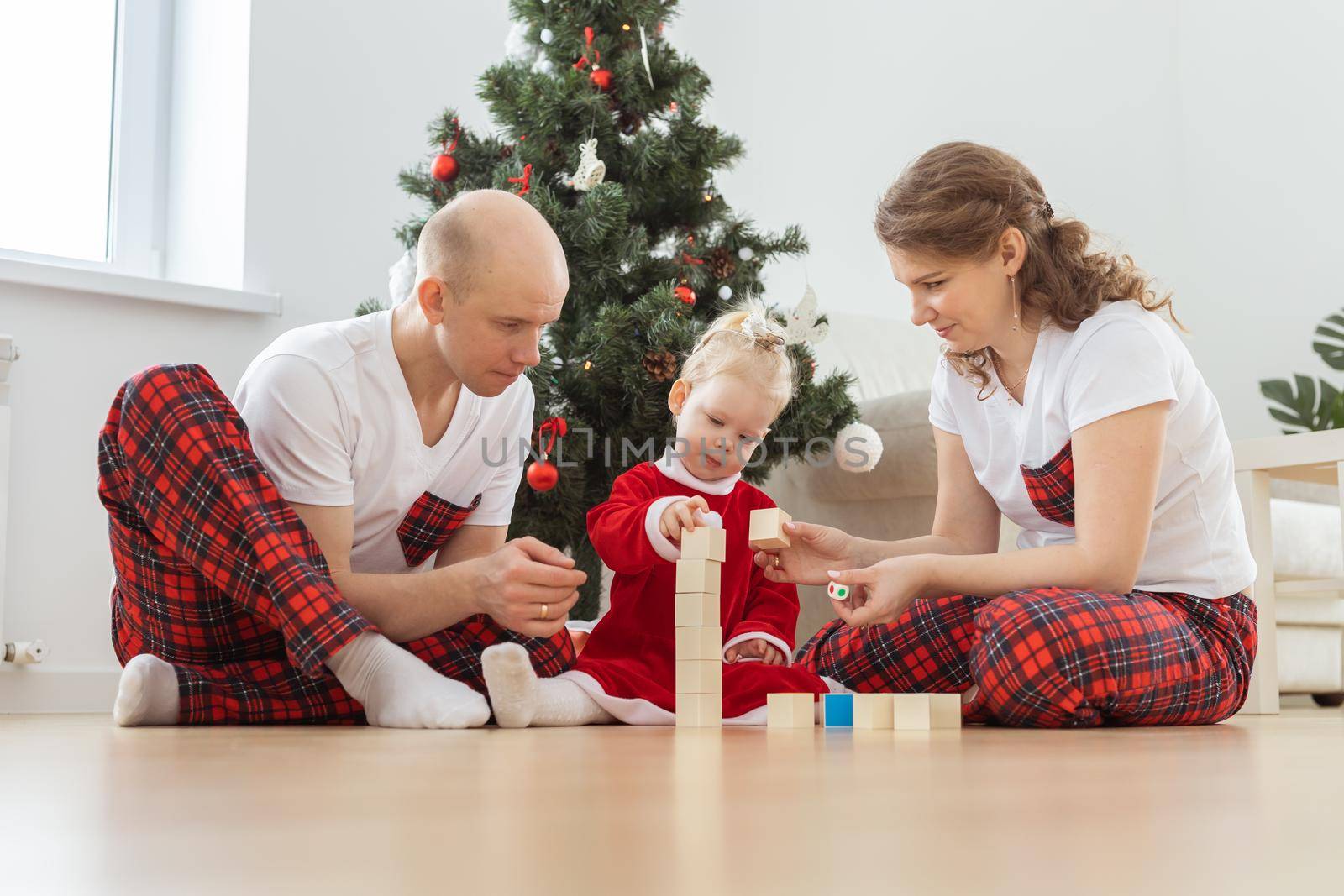 Toddler child with cochlear implant plays with parents under christmas tree - deafness and innovating medical technologies for hearing aid by Satura86