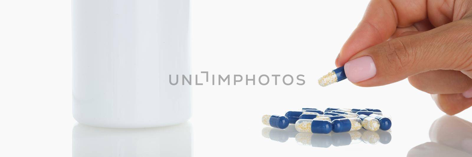 Close-up of female take one blue jelly capsule from bunch on surface. Plastic bottle with meds on table. Healthcare, treatment, recovery, pharmacy concept