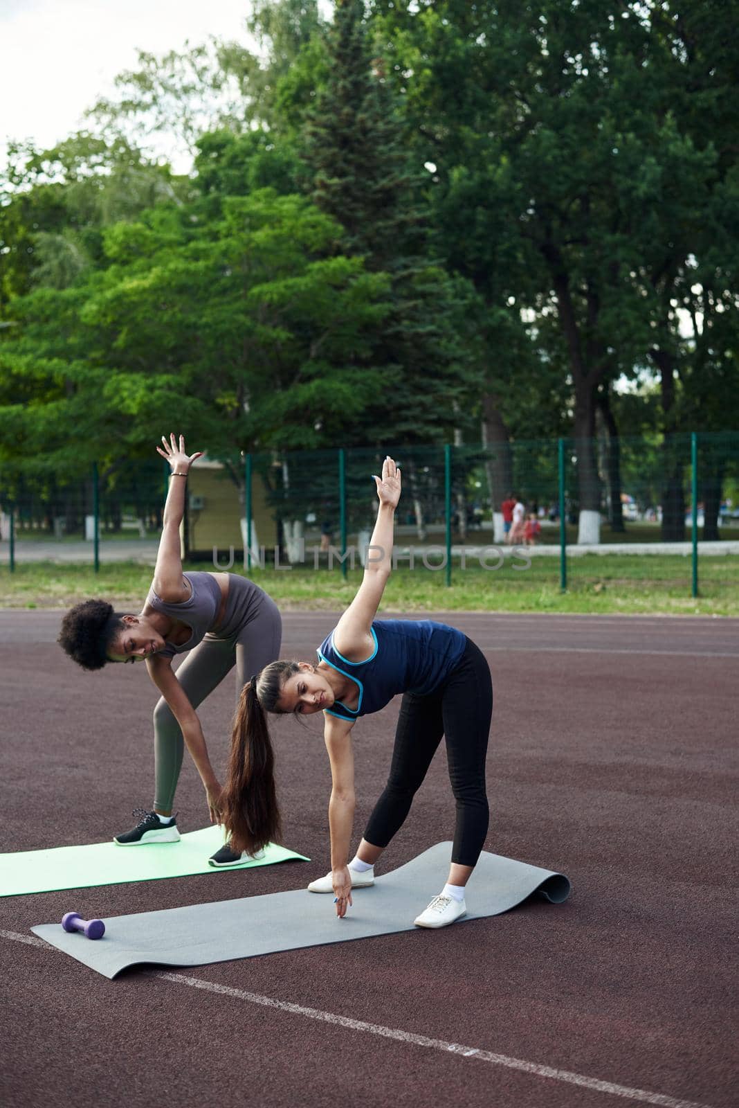 Two women of different nationalities warm up before training outdoors. Warming up muscles before strength training or jogging by etonastenka