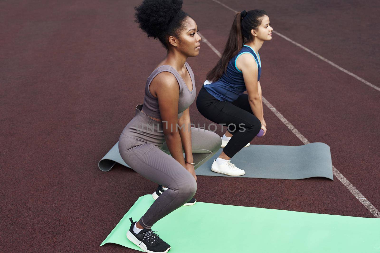 Two female friends do squats with dumbbells outdoors at the stadium