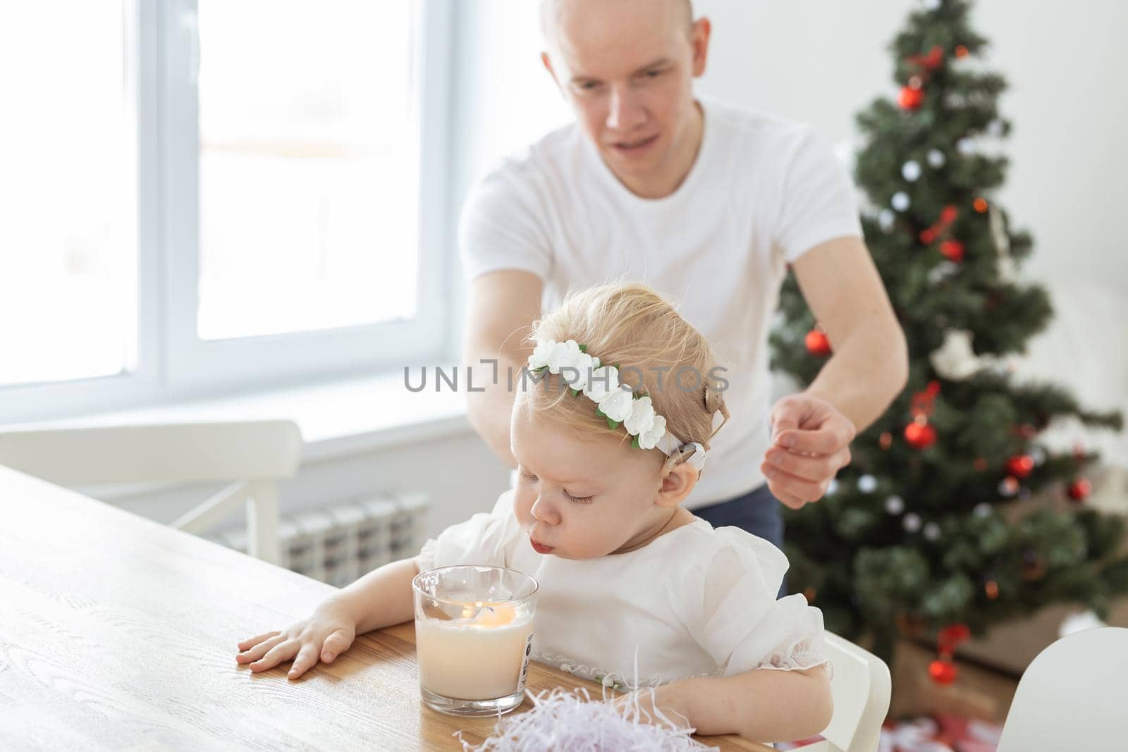 Father helps to put on cochlear implant for his deaf baby daughter in christmas living room copy space. Diversity and hearing aid and innovating medical technologies treatment deafness concept by Satura86