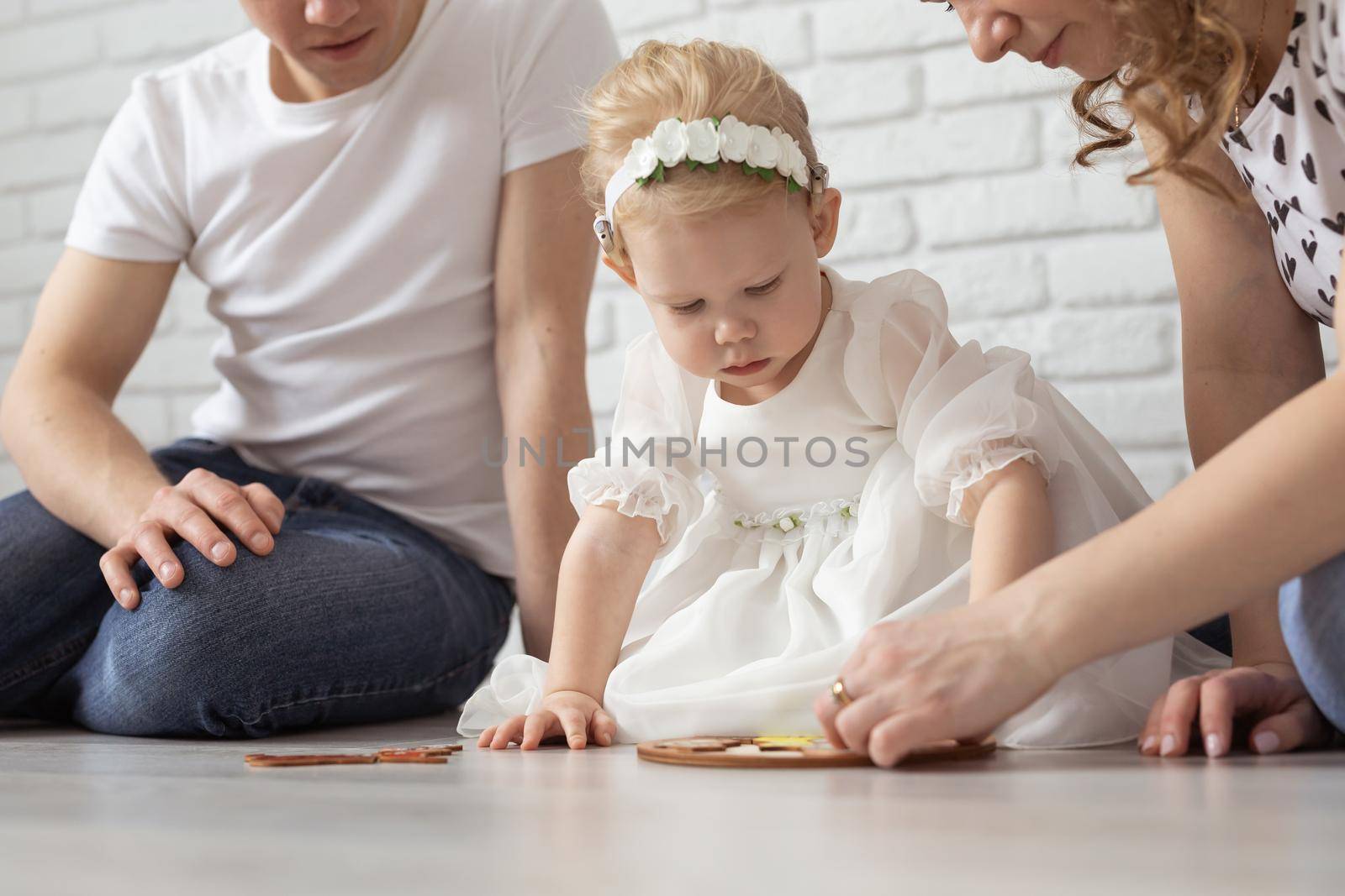 Baby child with hearing aids and cochlear implants plays with parents on floor. Deaf and rehabilitation and diversity concept by Satura86