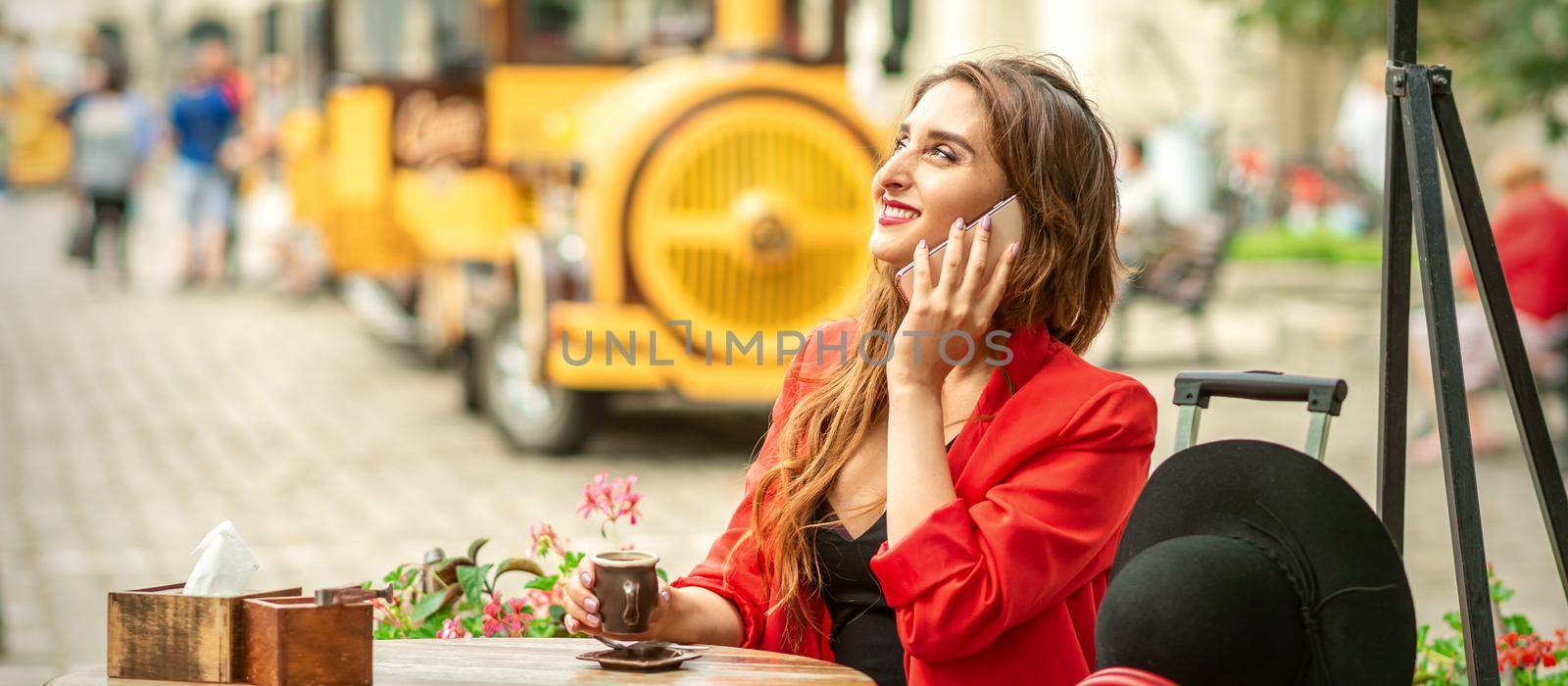 Beautiful happy young caucasian woman talking by cell phone sitting in outdoors cafe at european city