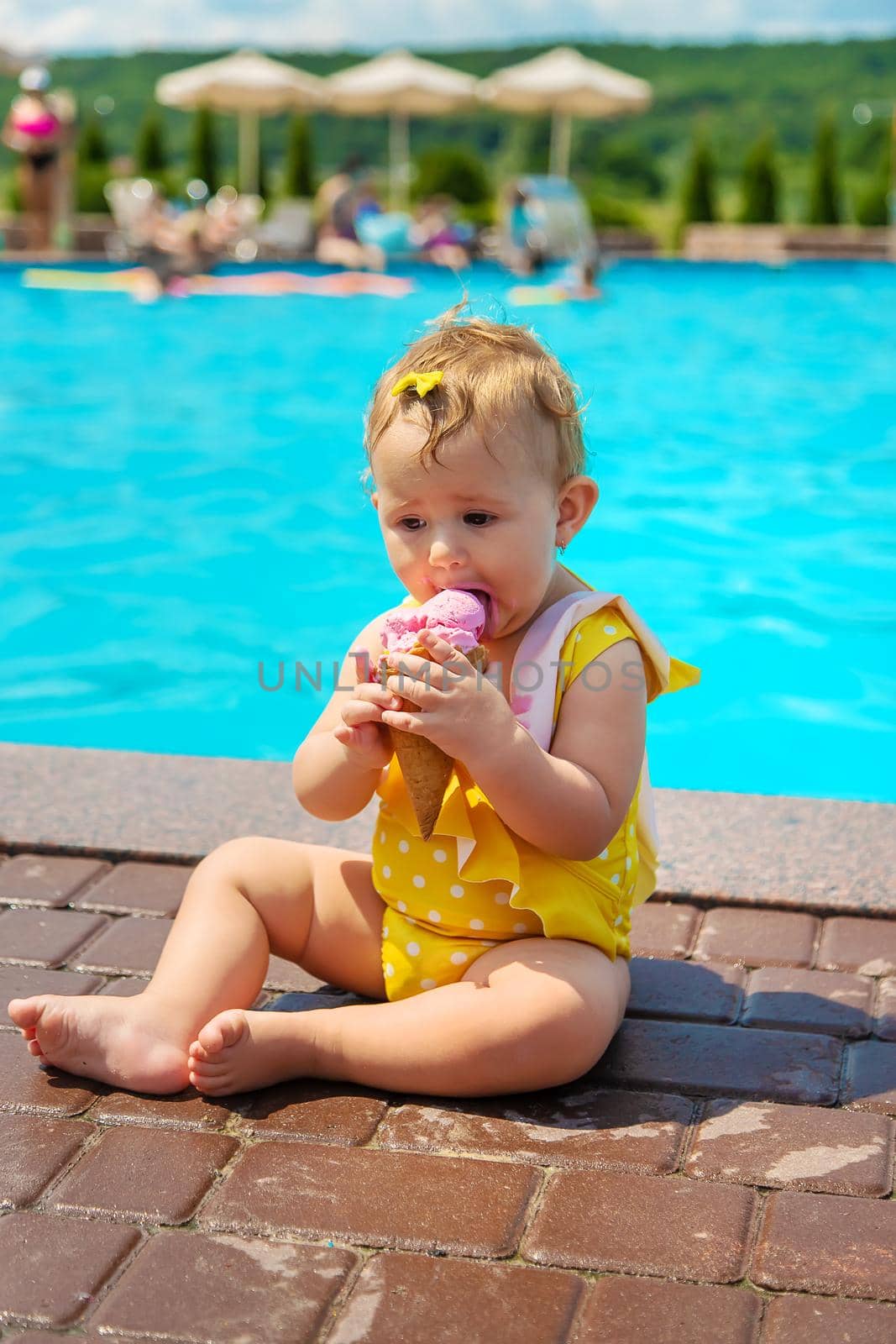 The child is eating ice cream near the pool. Selective focus. Kid.