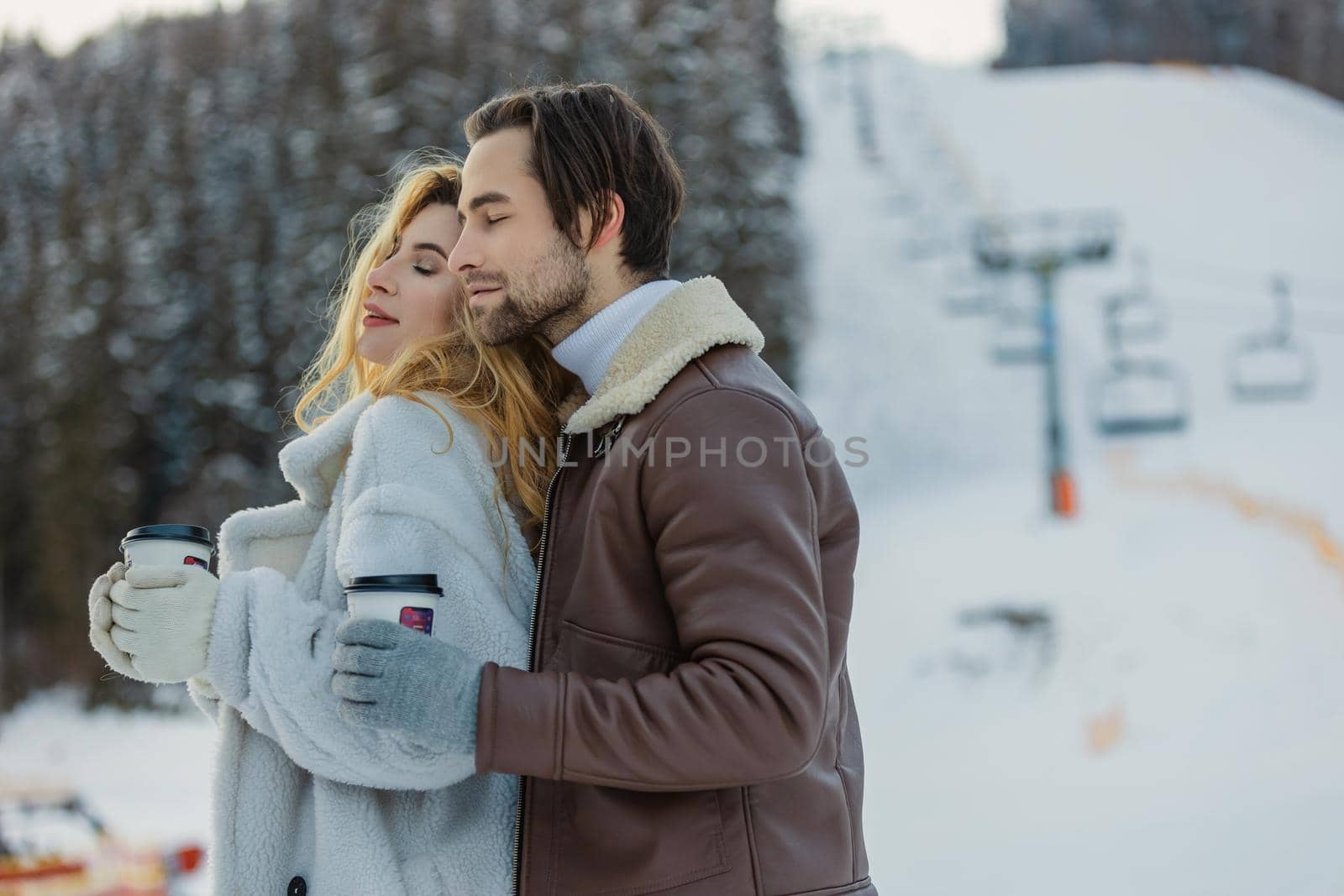 couple hugs and drinks coffee from disposable cups on the background of a snowy mountain