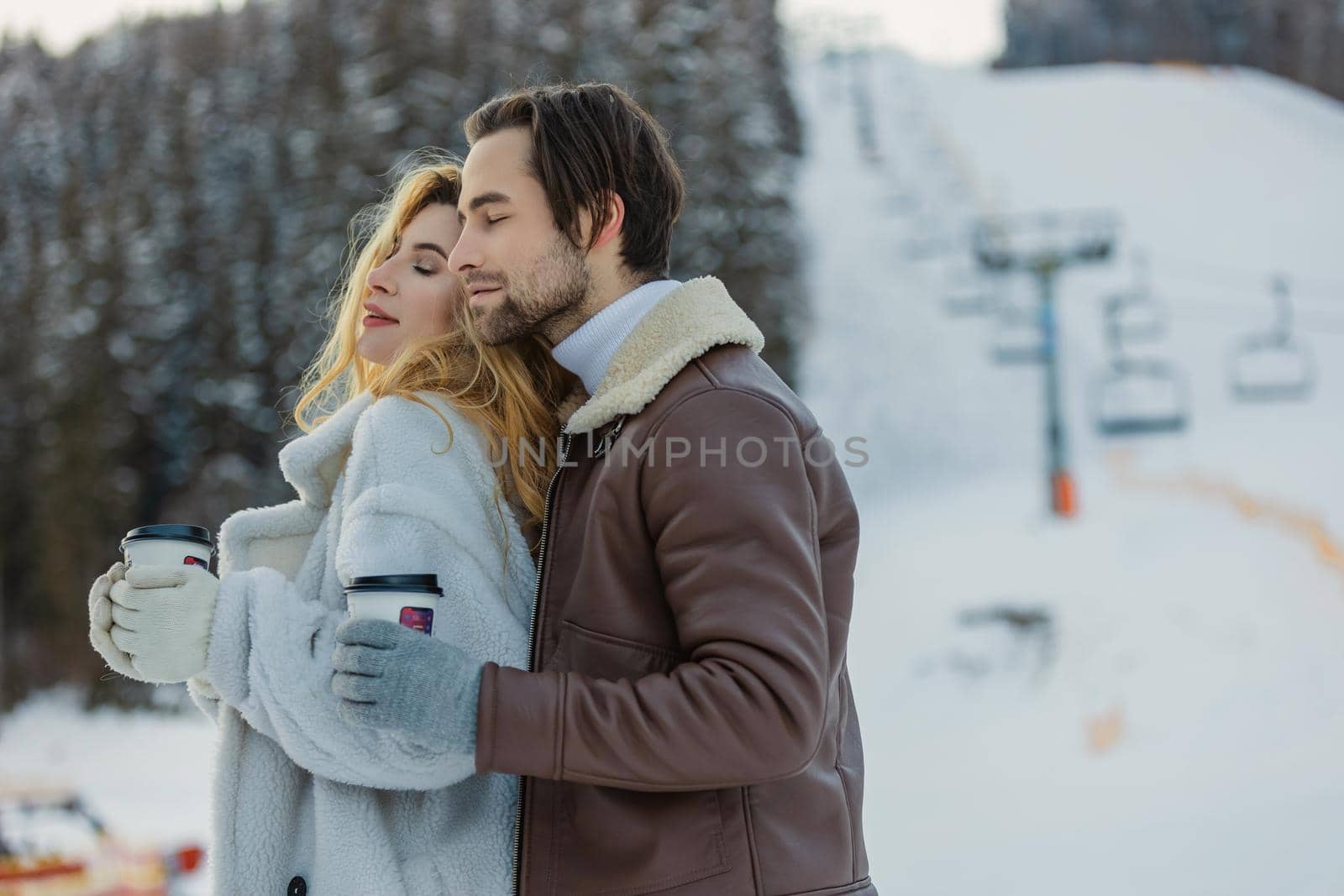 couple hugs and drinks coffee from disposable cups on the background of a snowy mountain
