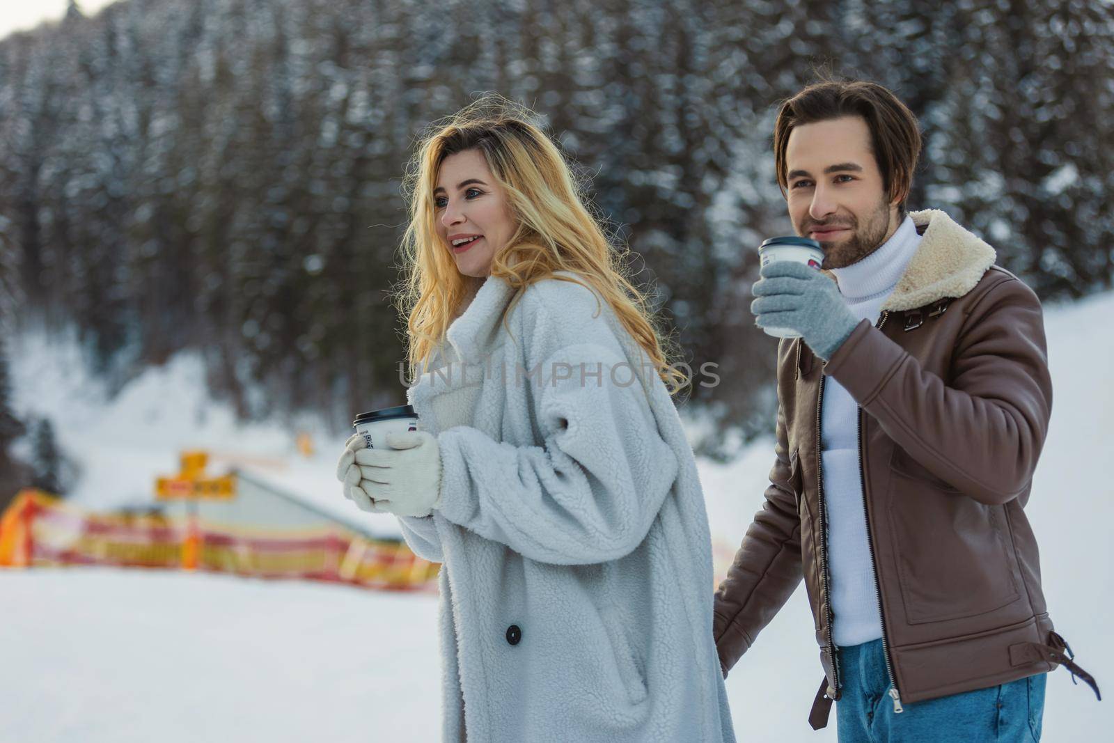 couple hugs and drinks coffee from disposable cups on the background of a snowy mountain