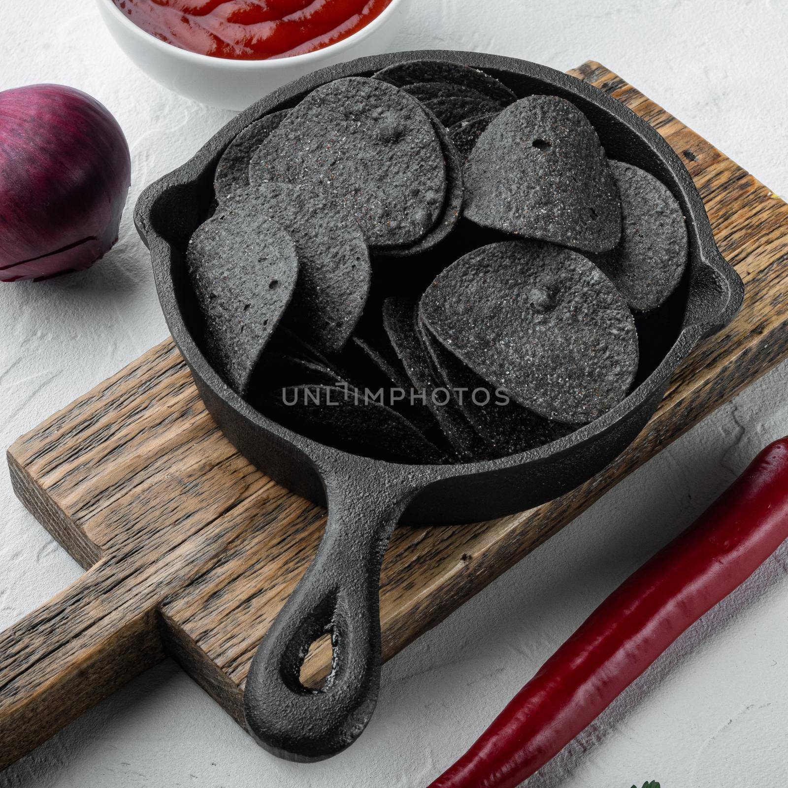 Black crispy potato chips set, in cast iron frying pan, on white stone surface
