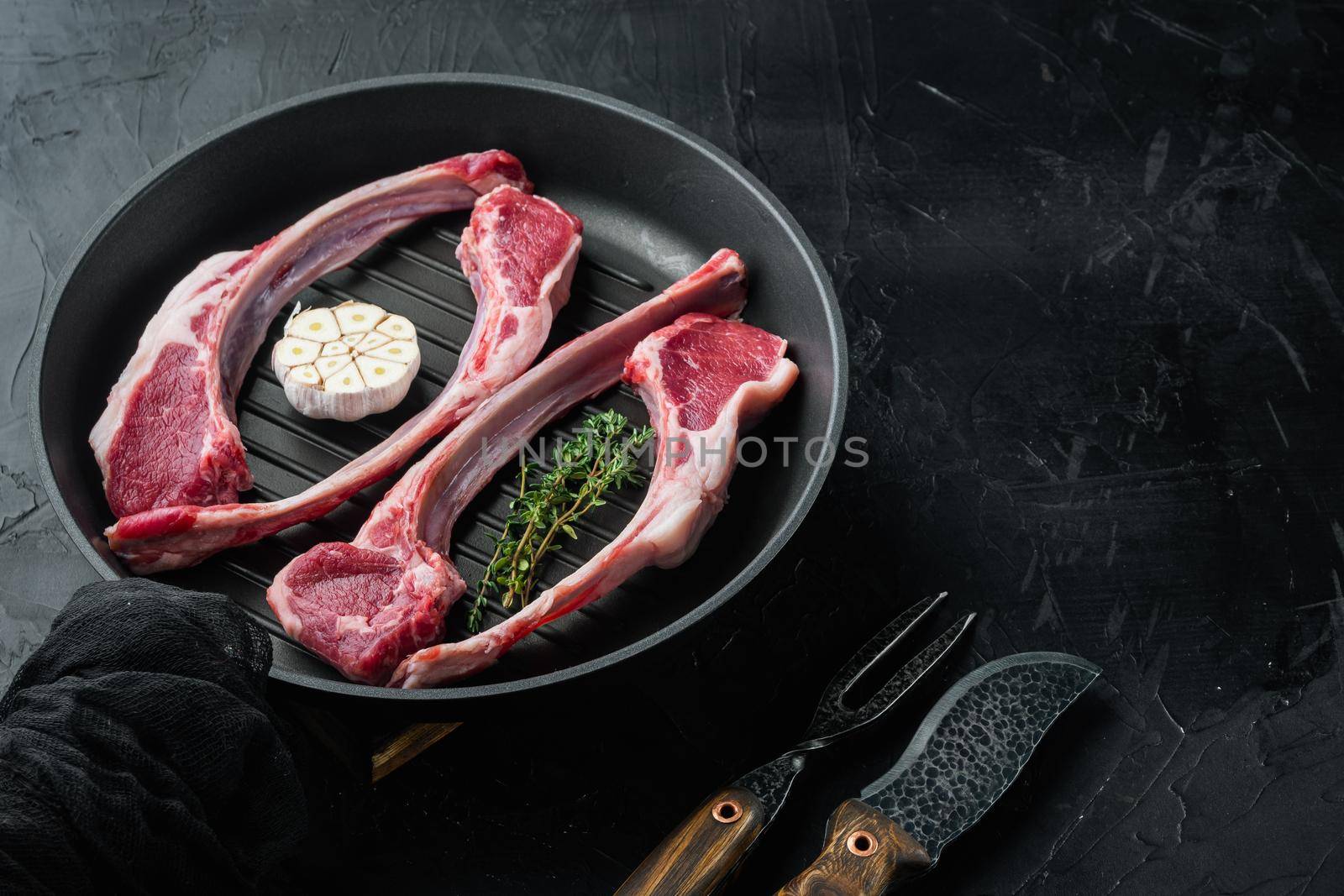 Organic pieces of mutton meat, Rack of lamb , raw with bone set, with ingredients, on frying cast iron pan, on black stone background , with copyspace and space for text