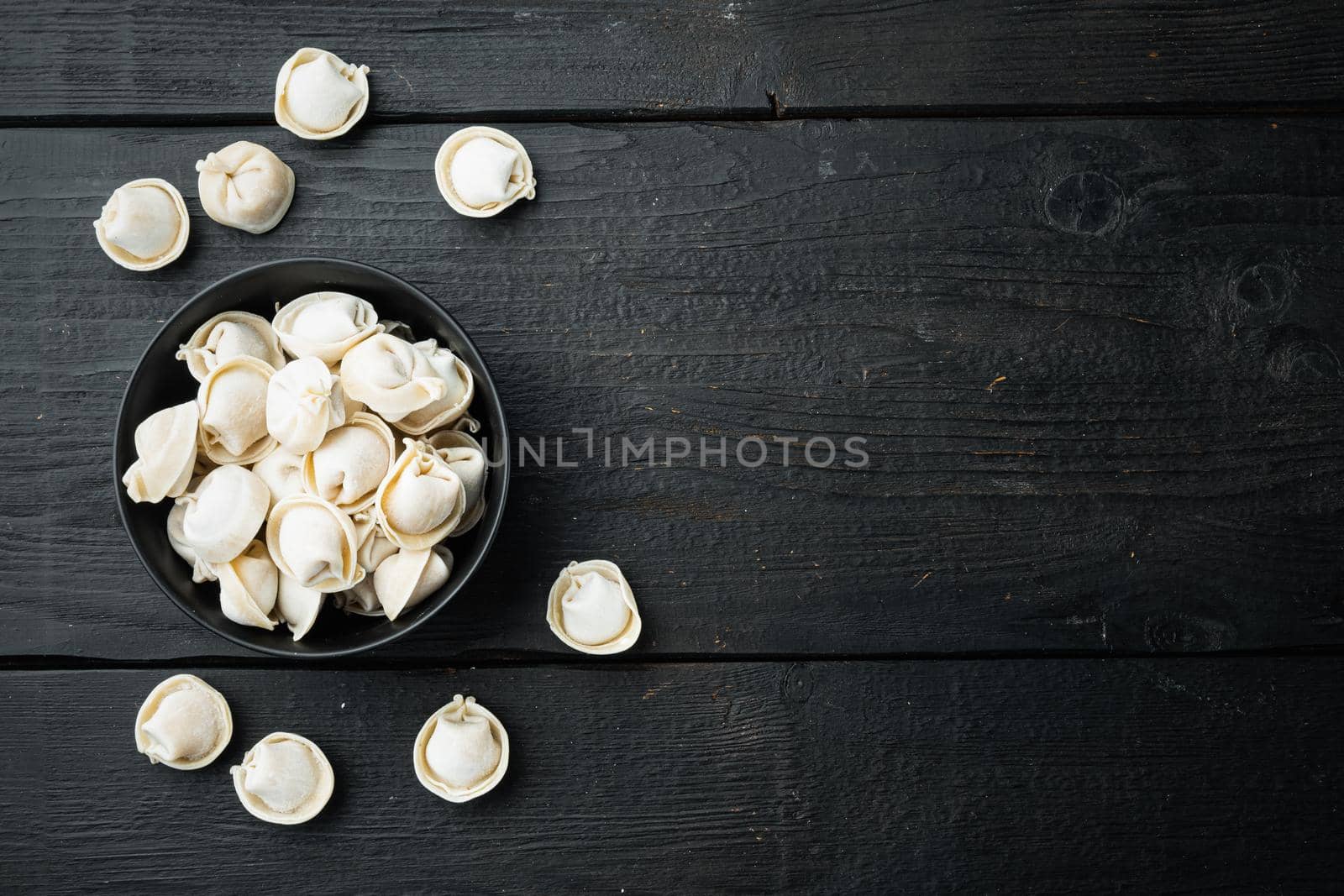 Frozen tortellini set in black bowl, on black wooden table background, top view flat lay , with copyspace and space for text