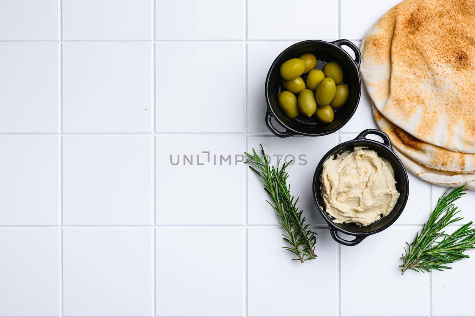Hummus and pita bread set, on white ceramic squared tile table background, top view flat lay, with copy space for text by Ilianesolenyi