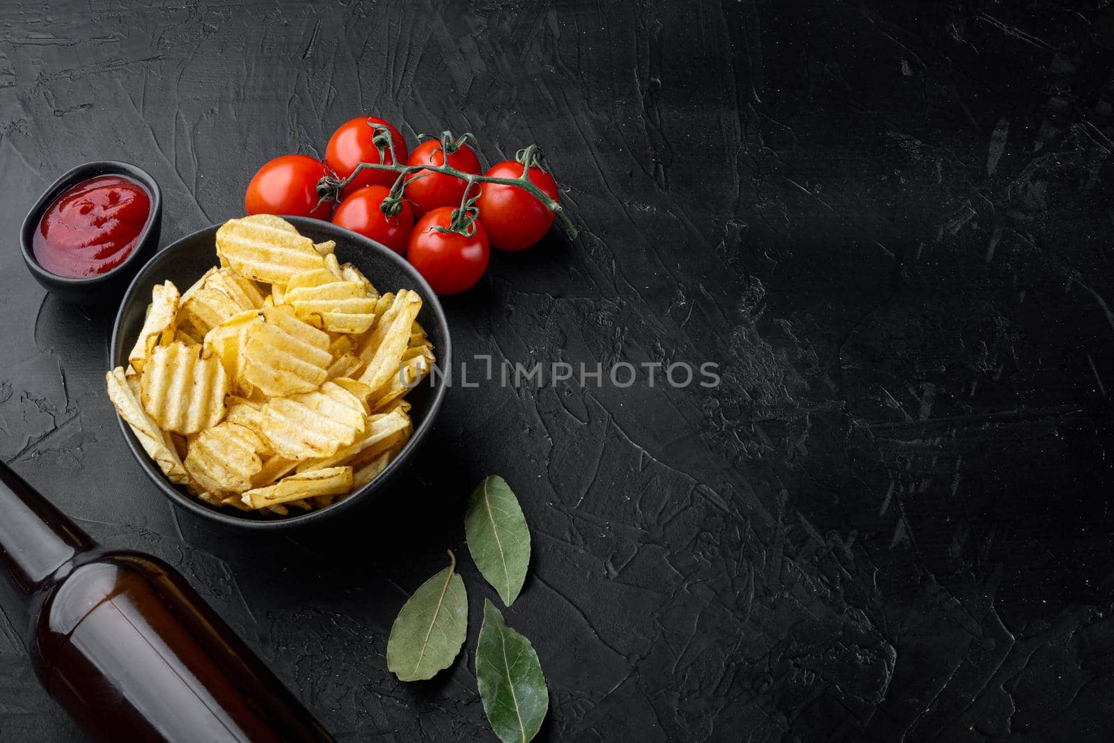 Crispy potato chips set, with bottle of beer, on black stone background, with copy space for text