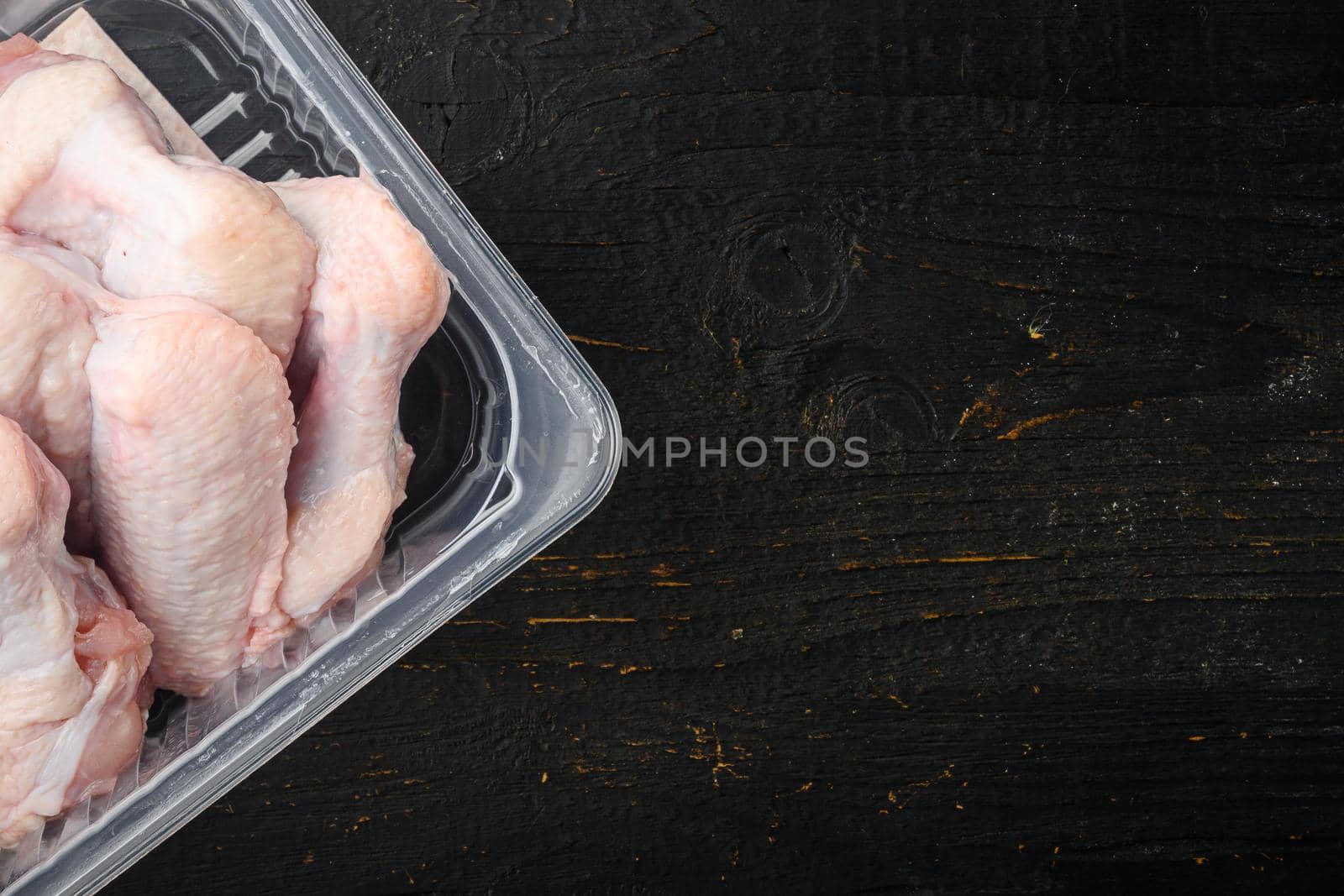 Raw chicken wings in plastic pack, on black wooden table background, top view flat lay, with copy space for text by Ilianesolenyi