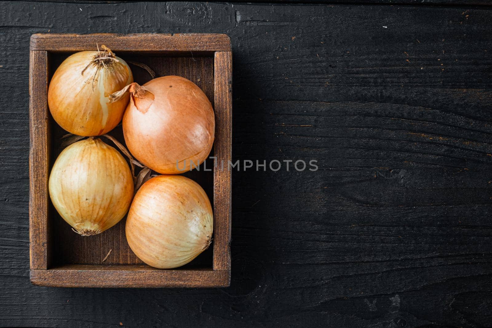 Unpeeled raw yellow onions, on black wooden table background, top view flat lay with copy space for text by Ilianesolenyi
