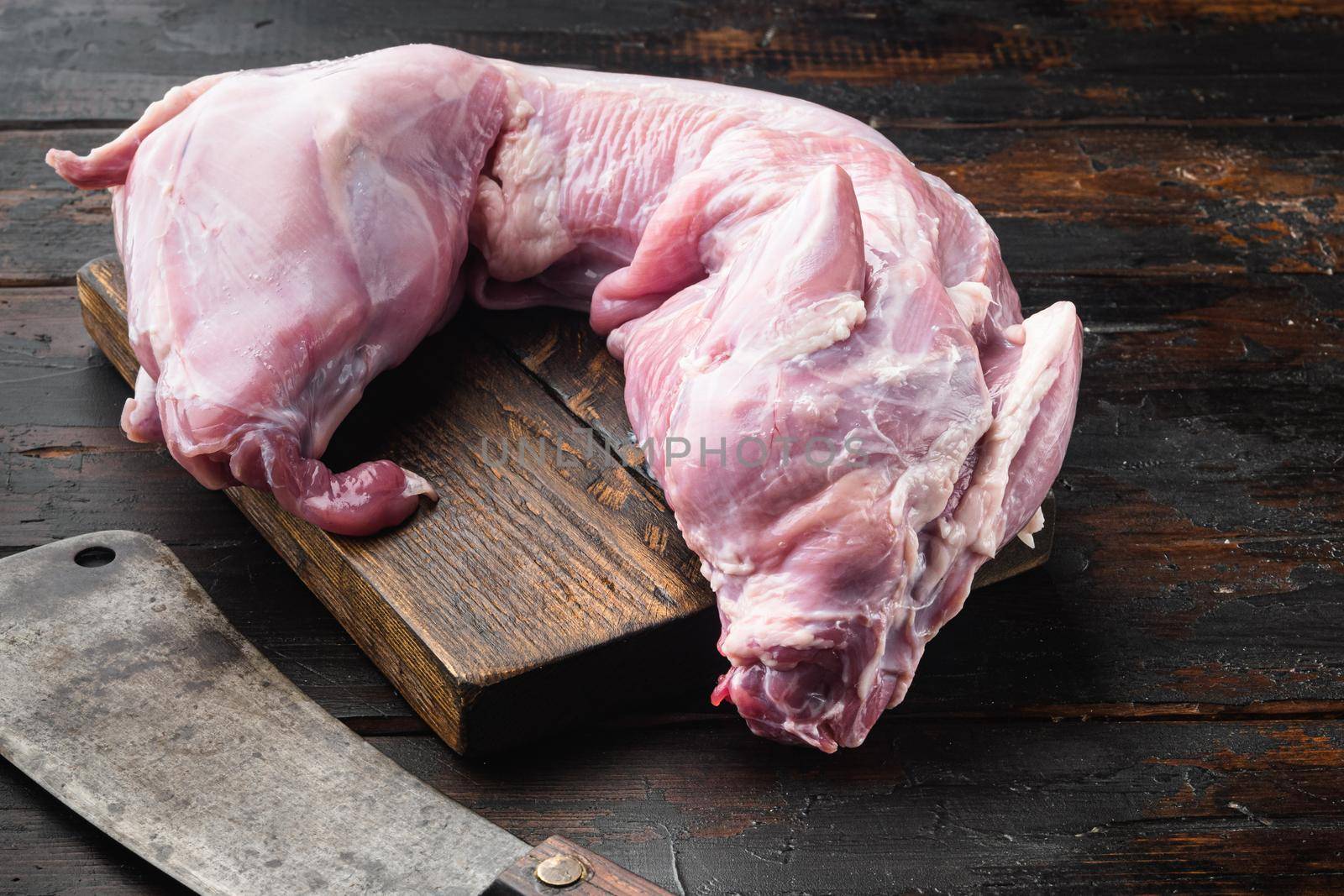 Raw fresh whole rabbit carcass set, and old butcher cleaver knife, on old dark wooden table