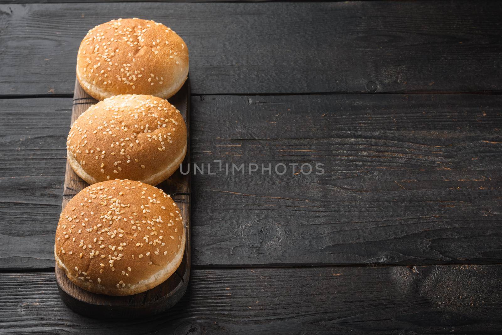 Fresh homemade burger buns with sesame set, on wooden serving board, on black wooden table background, with copy space for text