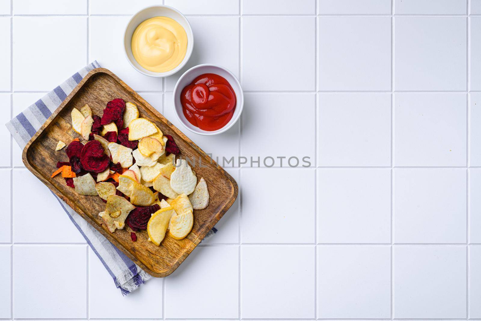 Dried vegetables chips, on white ceramic squared tile table background, top view flat lay, with copy space for text by Ilianesolenyi
