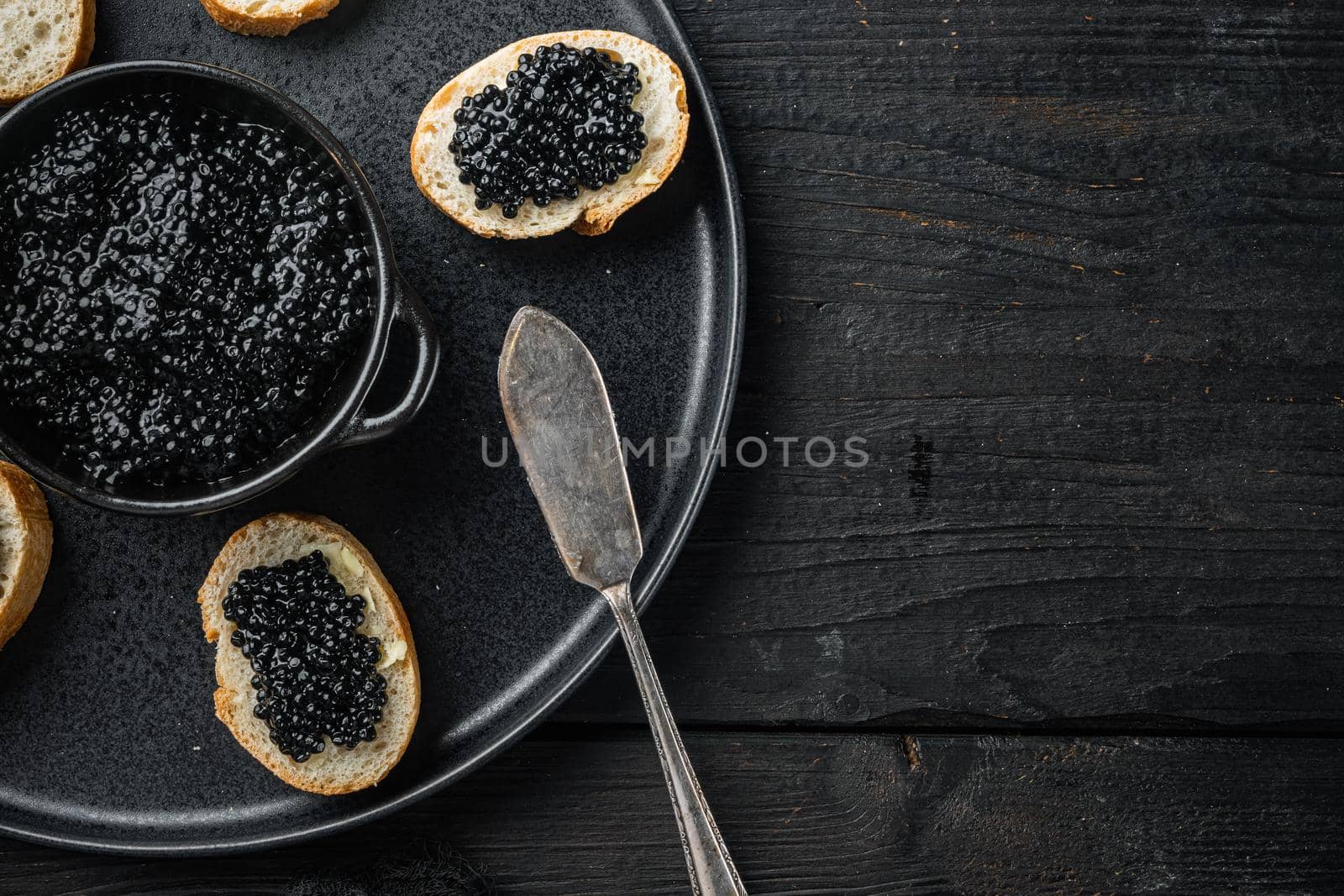 Sandwich with black caviar and butter, on black wooden table background, top view flat lay with copy space for text by Ilianesolenyi