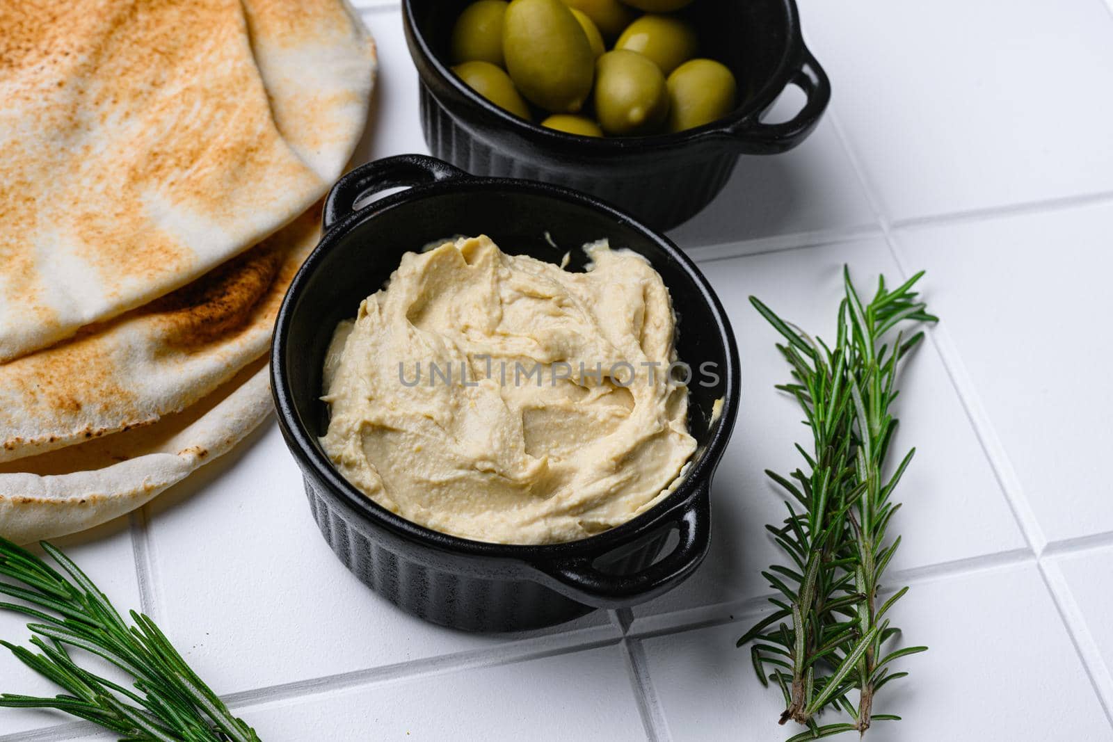 Bowl of tasty fresh hummus, on white ceramic squared tile table background