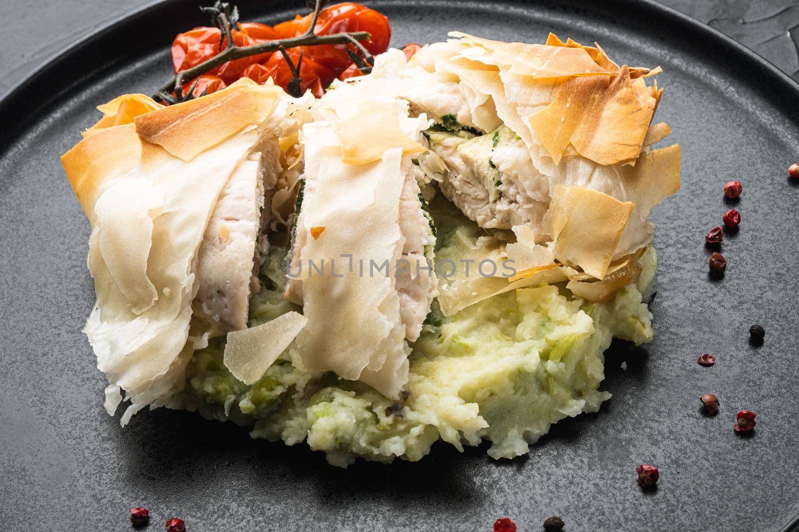 Chicken kiev filo set, with baked cherry tomatoes, mashed potatoes, on black stone background