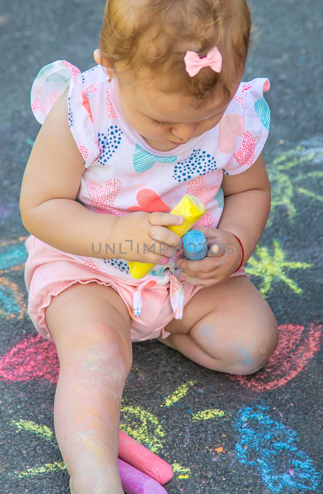 The child draws with chalk on the asphalt. Selective focus. by yanadjana