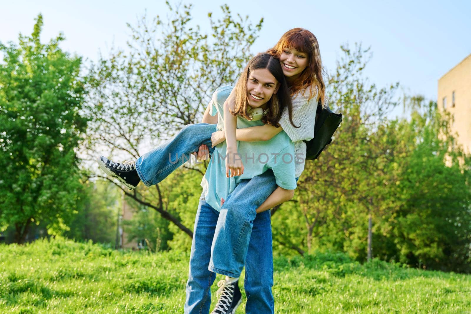 Couple of happy having fun teenagers together outdoor. Young teenage male and female laughing in park on lawn. Joy, happiness, friendship, summer, students, holidays, youth concept